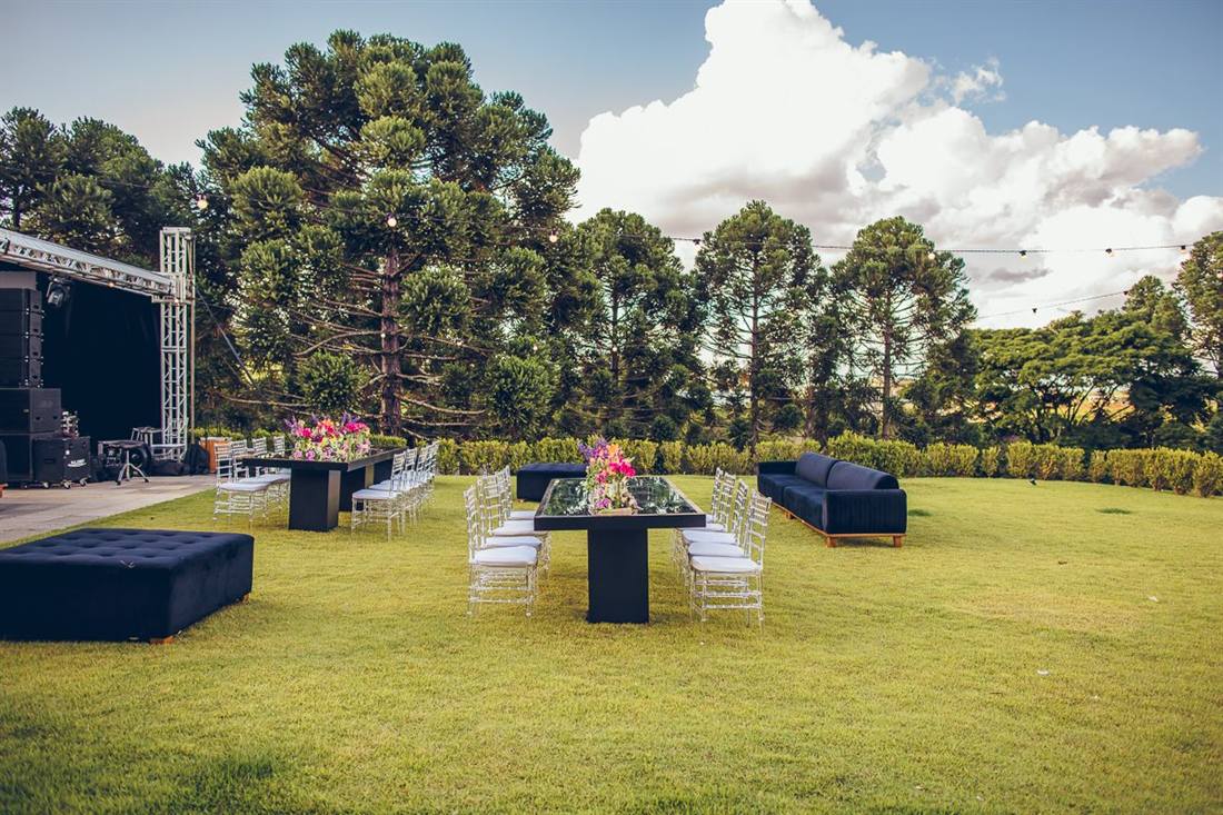 Gramado com mesas montadas para festa e araucárias ao fundo