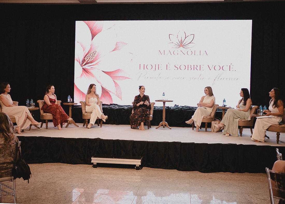 Mulheres conversando em poltronas no palco, com o telão do evento ao fundo
