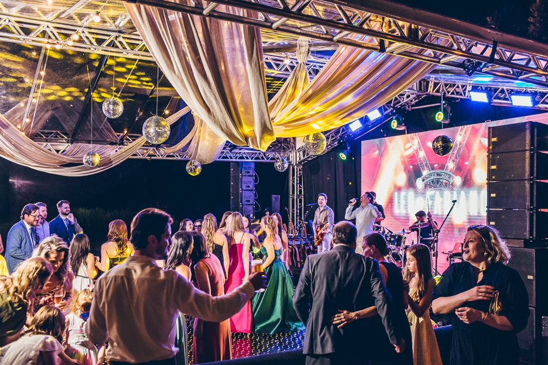 Banda no palco e pista cheia sob a tenda iluminada