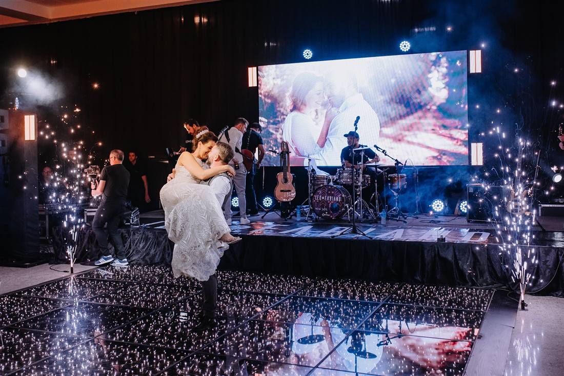 Noivos dançando na pista, com a banda e o telão no palco